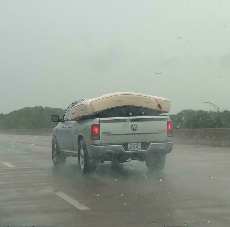 A pickup truck carrying a mattress in the rain on a highway, potentially an expensive mistake.