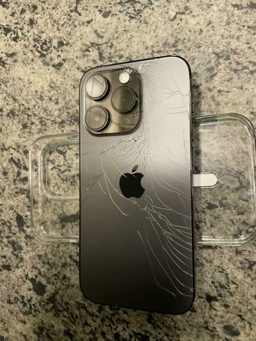 A broken iPhone lies on a counter, its back glass shattered, highlighting an expensive mistake and accident.