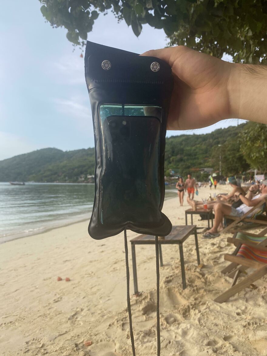 A person holds a wet phone in a waterproof pouch at a sunny beach, hoping to avoid an expensive mistake or accident.