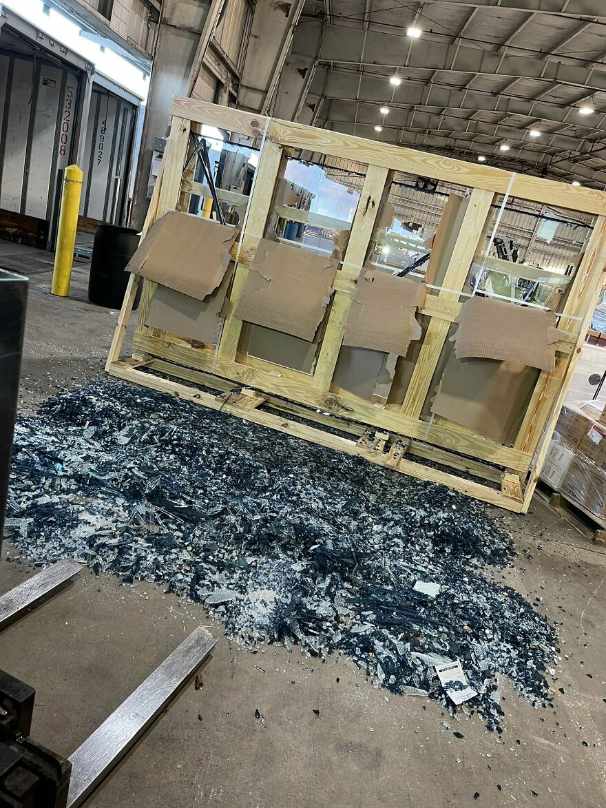 An expensive accident: shattered glass from a large wooden crate creating a pile of broken glass on a warehouse floor.