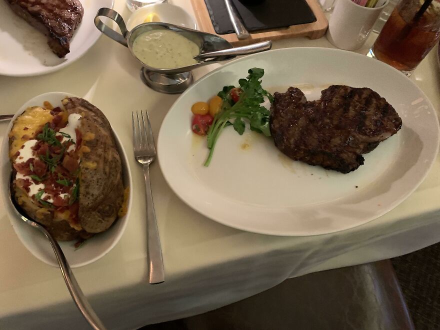 A culinary mistake: a well-cooked steak with a loaded baked potato and a side of greens, an expensive restaurant meal.