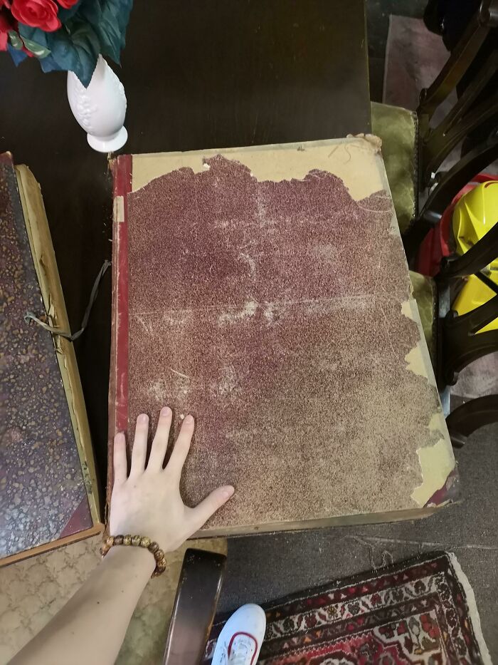 A human hand rests on a massive old book, highlighting the true scale of the antique volume.