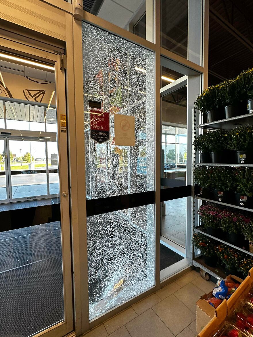 A shattered glass door at a store entrance, showing an expensive accident, with merchandise visible inside the store.