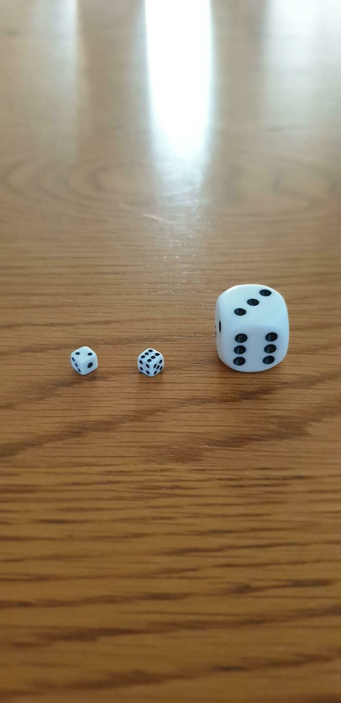 Three dice of vastly different sizes on a wooden table, providing a clear size comparison and true scale.