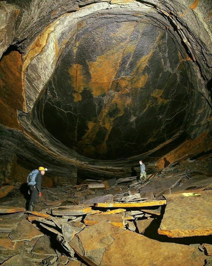 A cavern interior revealing the true scale of a large rock formation with two people for size comparisons.