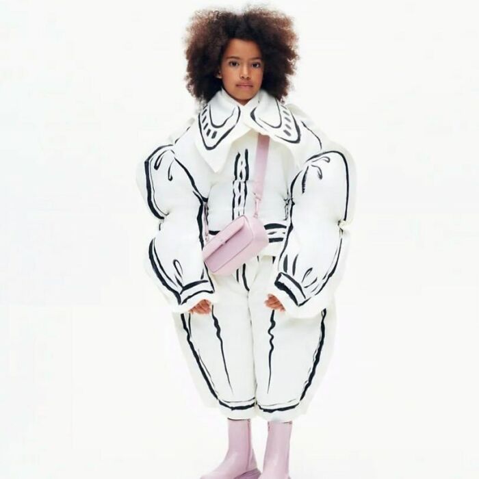 A child in bizarre content from Zara website, wearing an oversized white puffy suit with black outline details.