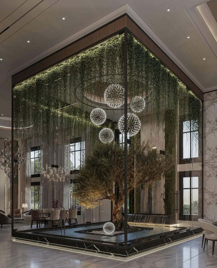 An indoor garden with a large tree in a glass enclosure, surrounded by hanging greenery and spherical chandeliers, showcasing brilliant design.