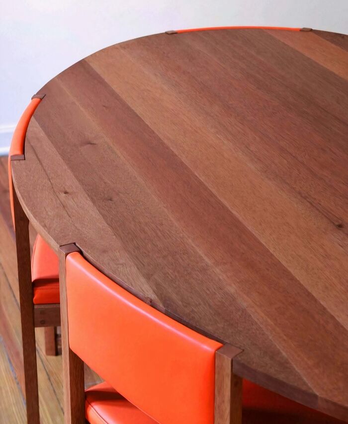 Brilliant design choices: A close-up of a round wooden table with orange chairs, showcasing integrated design details.
