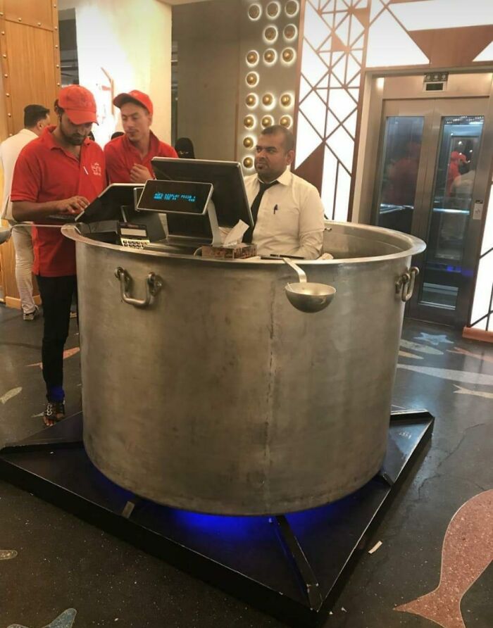 A restaurant host seated inside a giant cooking pot, brilliantly transformed into a unique reception desk, making it more enjoyable.