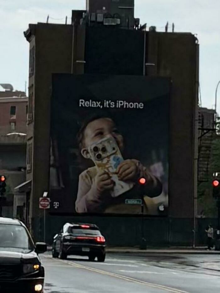 A billboard showing a baby chewing on an iPhone, highlighting consumerism and price difference.
