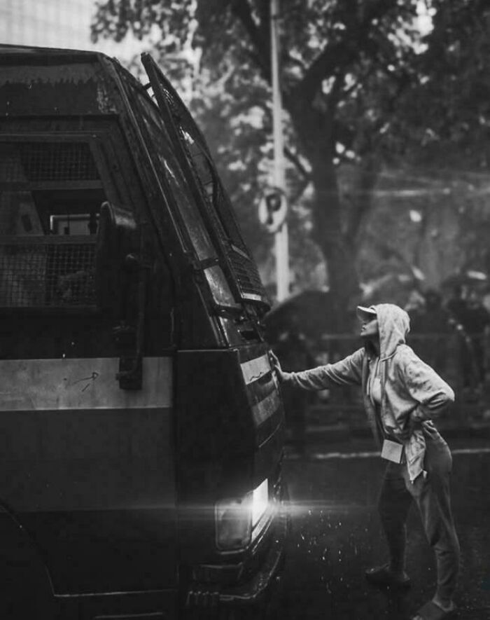 A chaotic good post showing a person in a hoodie interacting with a large vehicle in the rain.