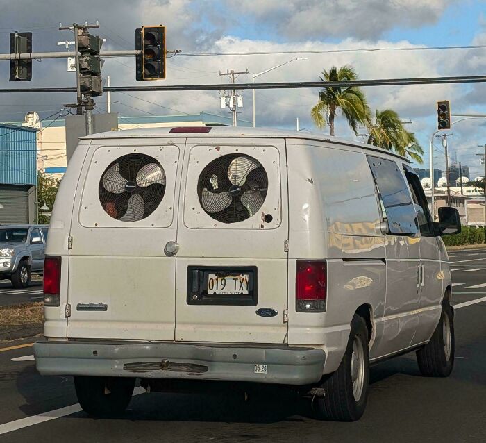 A white van with two large fans installed in the rear windows, a clever solution for ventilation using random junk.