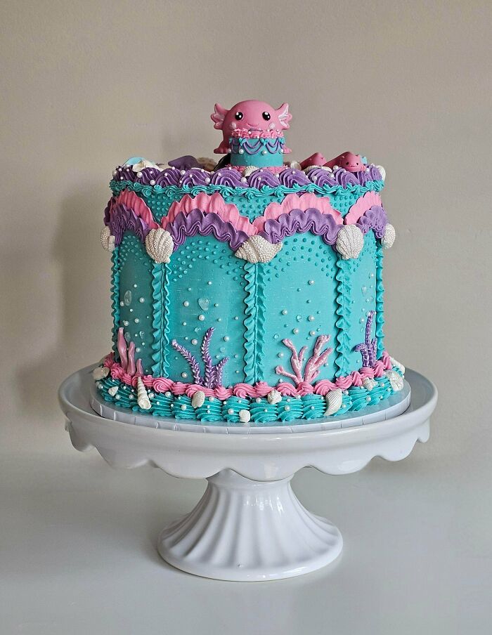 An elaborate blue, pink, and purple underwater-themed cake with a cute axolotl, an amazing baked treat.