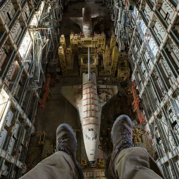 A pair of boots dangling above a large, derelict space shuttle inside a crumbling hangar, an unexpected find for urban explorers.