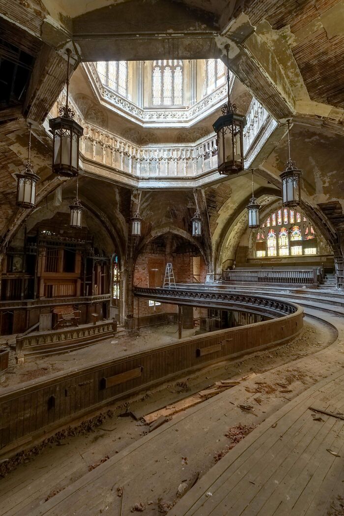 Urban explorers exploring an old, abandoned church with ornate architecture, stained-glass windows, and a circular balcony.