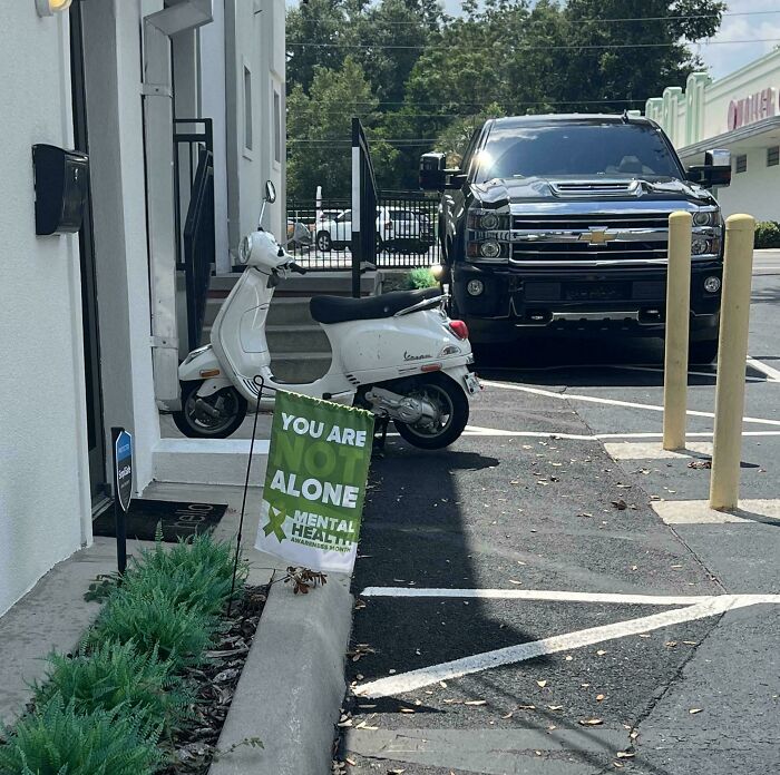 An awful design fail: a You Are Not Alone Mental Health Awareness sign partially hidden behind a parked scooter.