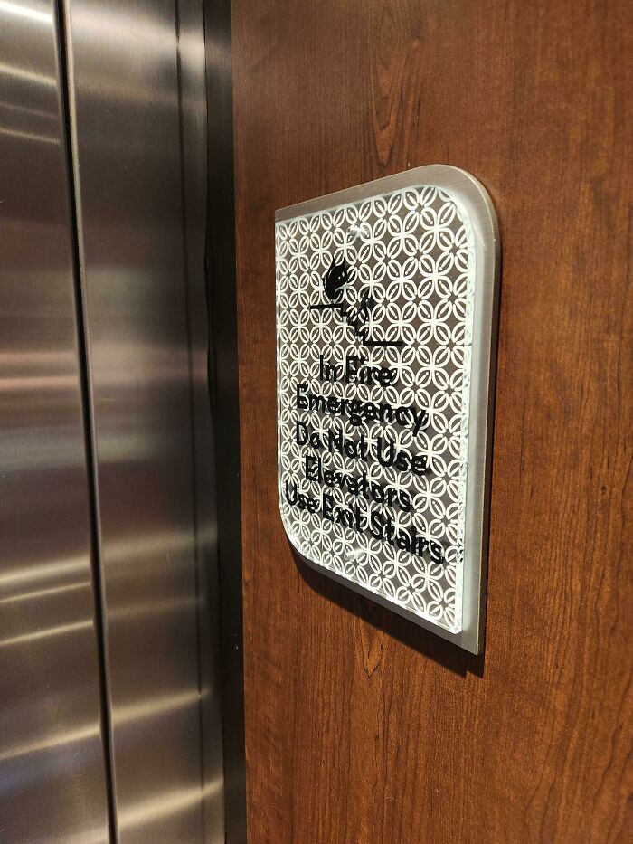 A dark wood and metal sign with a hard-to-read patterned overlay, an awful design fail for an elevator.