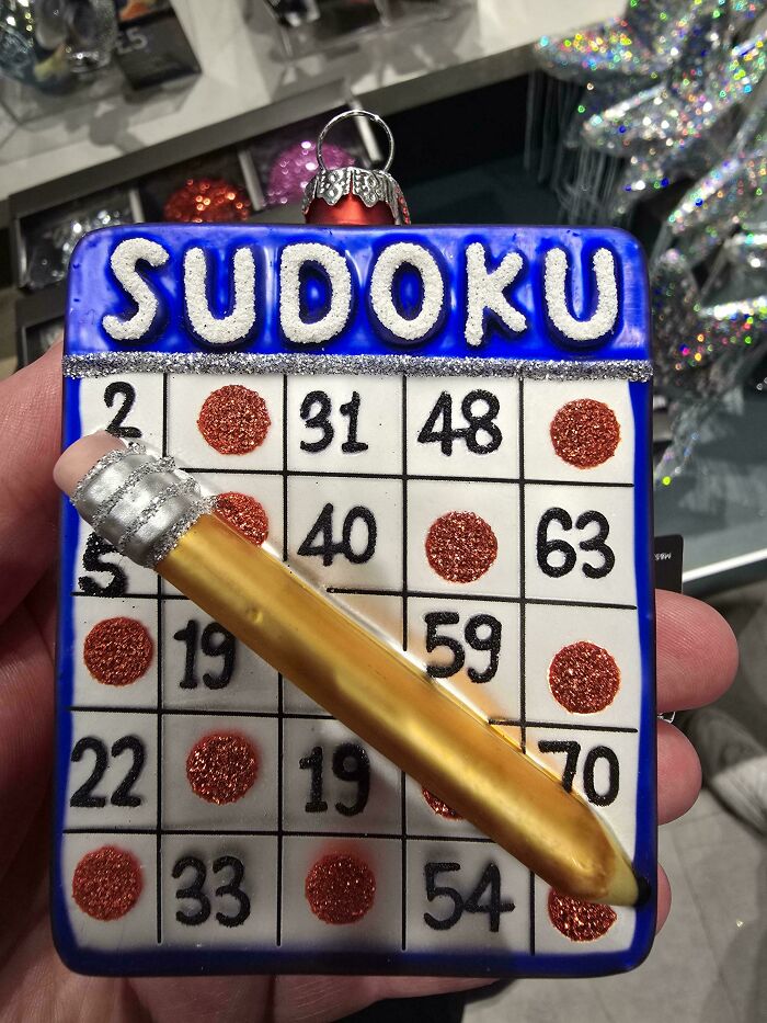 A hilariously awful design fail Sudoku bingo card Christmas ornament with a pencil, displaying numbers and red glitter circles.