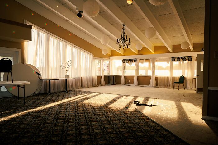 A sunlit, dusty event hall with a chandelier and white paper lanterns, an unexpected find for urban explorers.