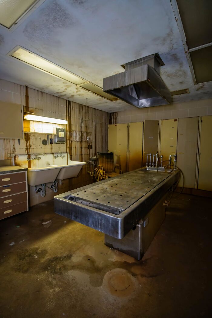 An abandoned mortuary room with two sinks and a metal examination table, an unexpected find for urban explorers.