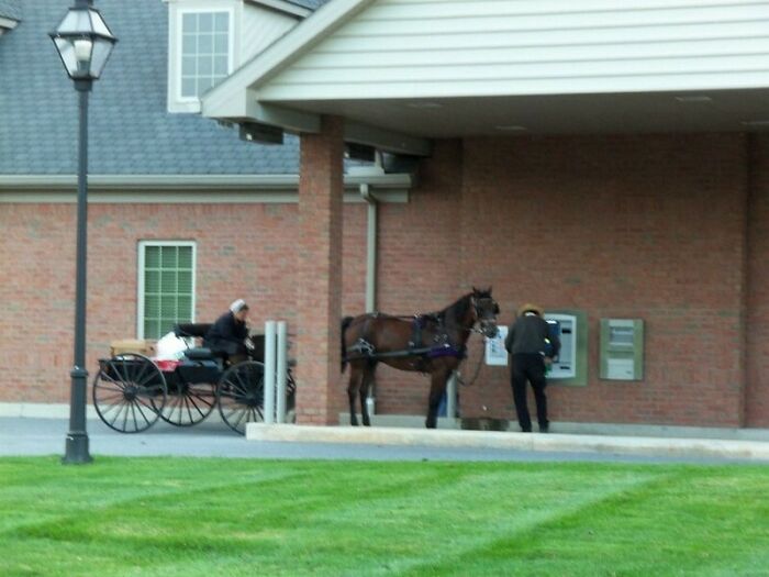 An Amish buggy and horse parked at an ATM, with a person using the machine, illustrating different photos of USA.