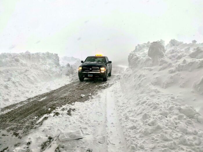 Photos of the USA: a pickup truck driving through a road carved between towering snowdrifts during a severe winter storm.