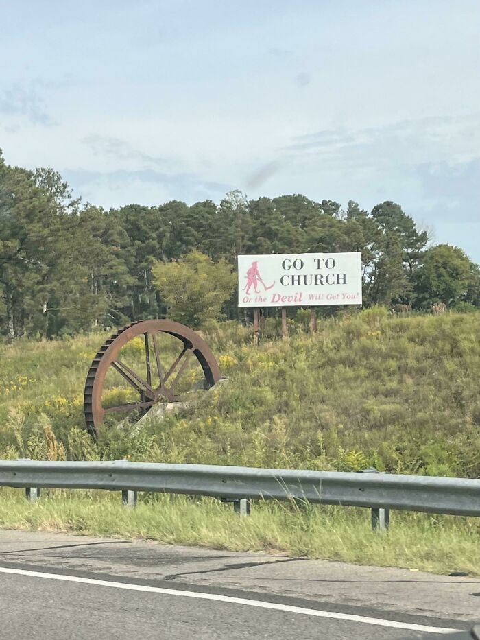 Photos of the USA: a peculiar billboard in a grassy field that reads Go To Church or the Devil Will Get You! with an old rusty water wheel nearby.