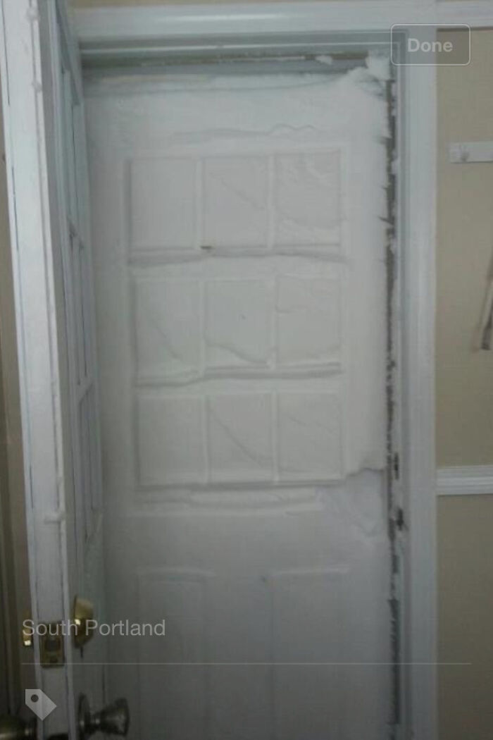 A white door is completely covered in a thick layer of snow and ice, blocking the entrance from the outside, showing different photos of the USA.