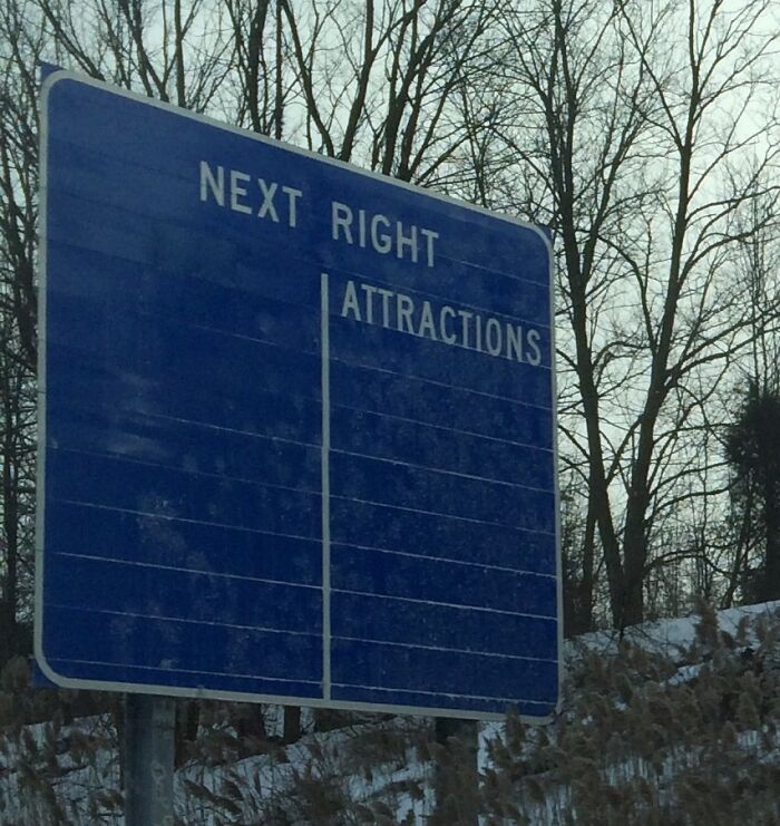 A blue highway sign in the USA with the words NEXT RIGHT and ATTRACTIONS, against a backdrop of trees and snow.