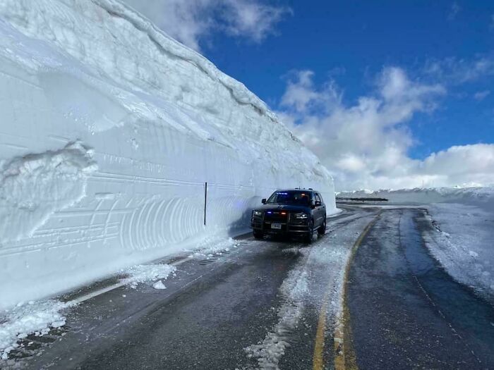 A vehicle driving on a road carved through immense snow walls in the USA, highlighting different photos of the USA.