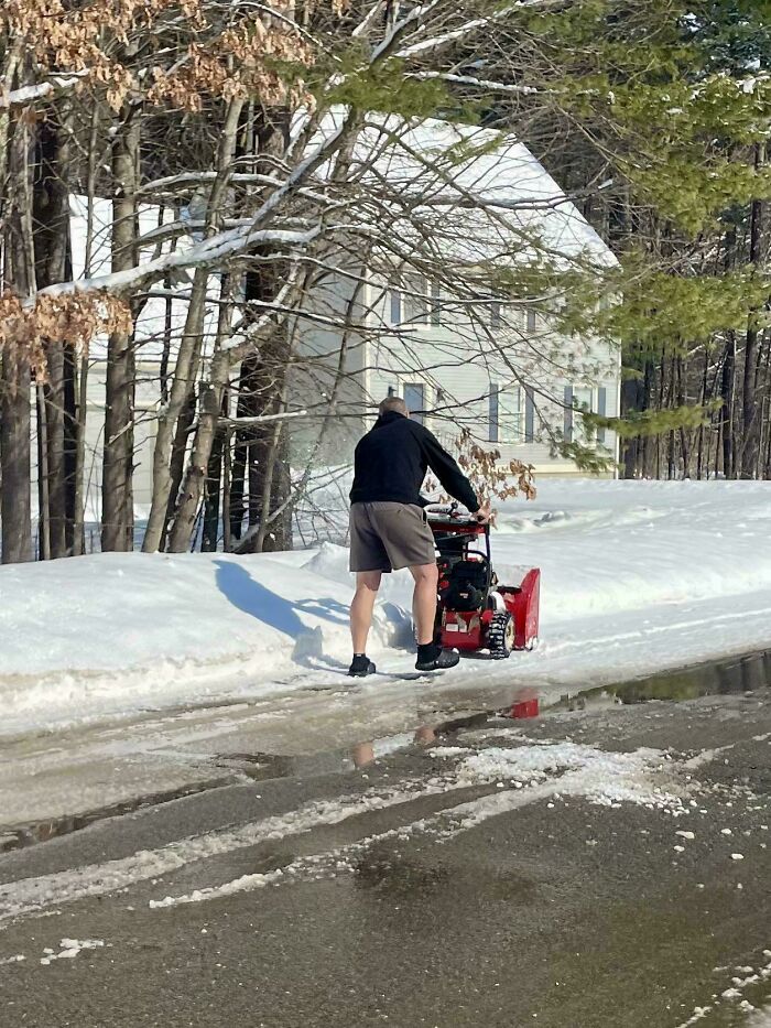 A man in shorts clears snow with a snowblower in the USA, showing a fascinating and different photo.
