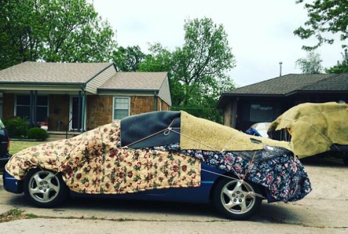 A blue car covered in various blankets and tied down with ropes, a strangely fascinating photo of the USA.