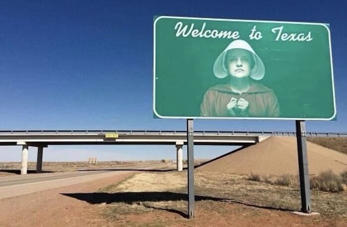 A Welcome to Texas sign featuring a figure from The Handmaids Tale, offering a fascinating and wildly different photo of the USA.