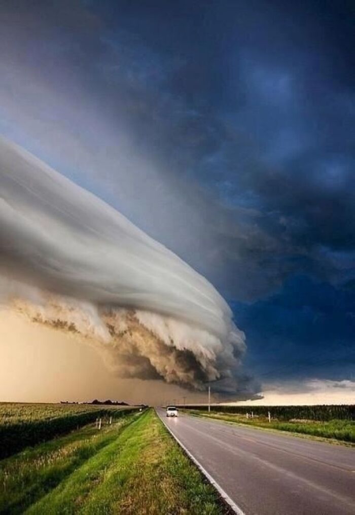 A powerful storm cloud stretches across the sky over a long, empty road, showcasing a fascinating and wildly different photo of the USA.