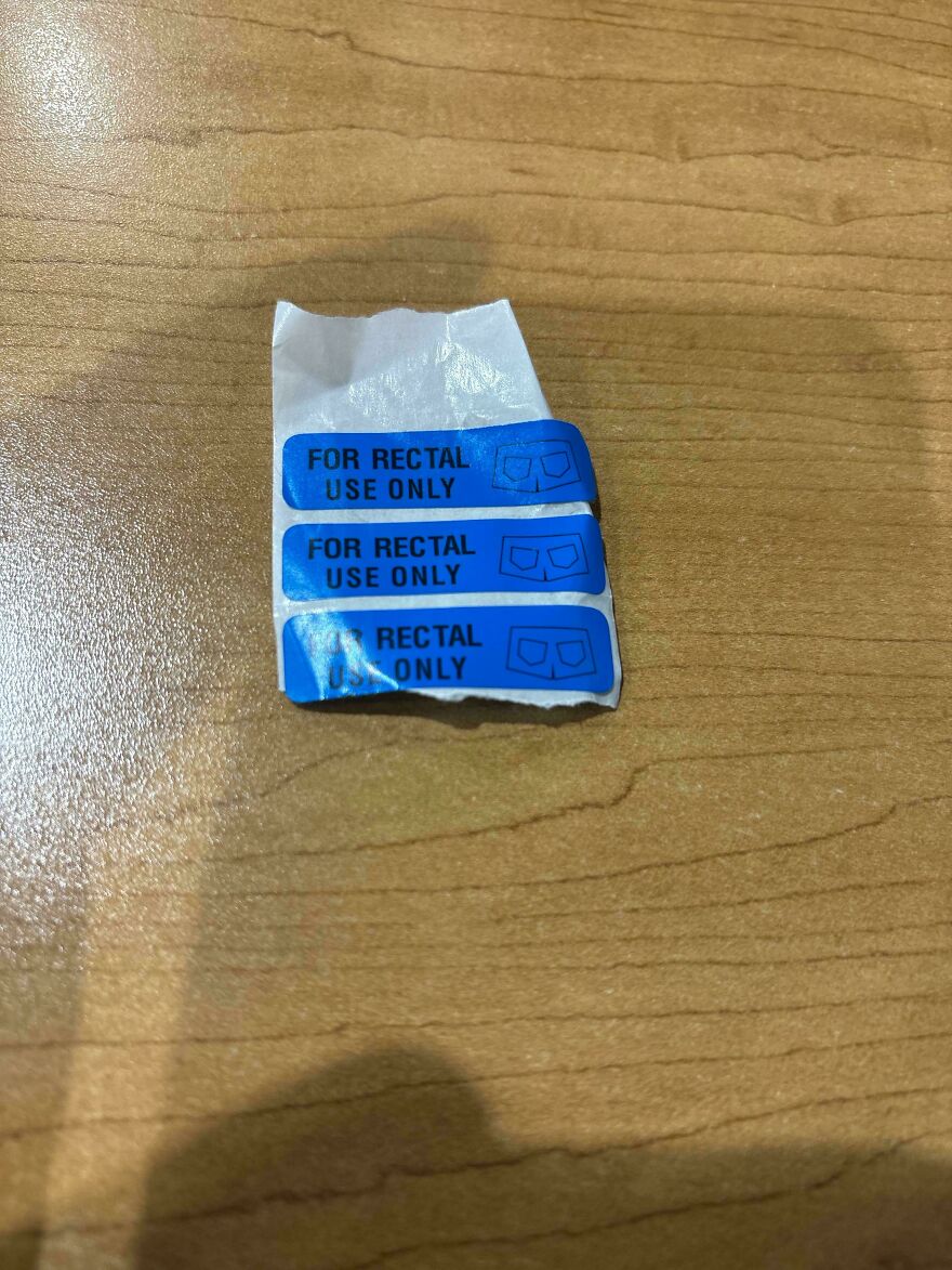 Three small blue and white stickers on a wooden surface, each reading FOR RECTAL USE ONLY, an amusing thing.
