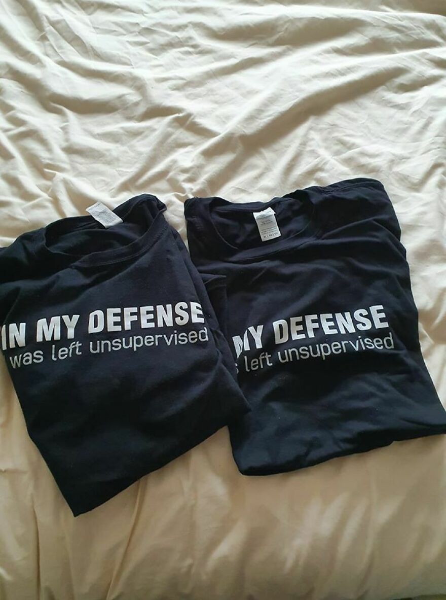 Two black t-shirts laid on a bed with the slogan 'IN MY DEFENSE I was left unsupervised,' an amusing thing.