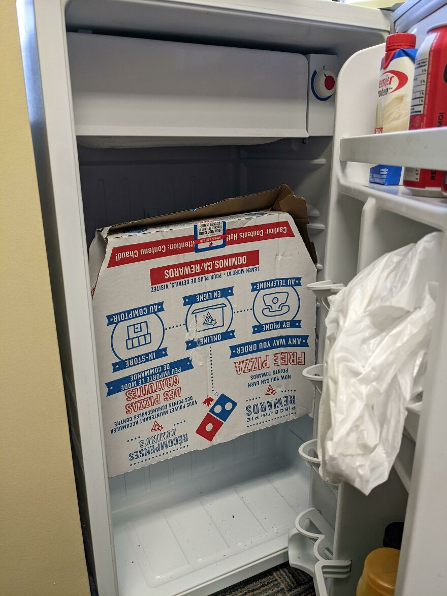 An open refrigerator with a large pizza box awkwardly stuffed inside, one of the mildly amusing things.