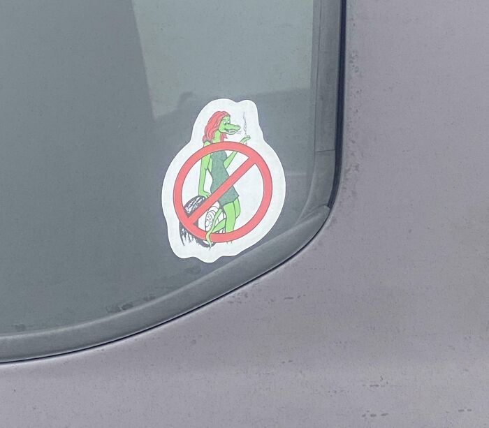 Funny bumper sticker showing a no smoking symbol over an alligator woman on a car window.