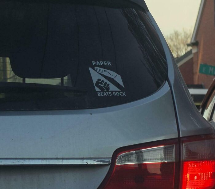 Wild bumper sticker on a car's rear window, Paper beats rock in a rock-paper-scissors game.