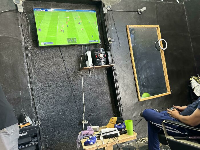 A surprisingly simple and genius idea, a barber shop with a TV playing a soccer game and a person playing a video game.