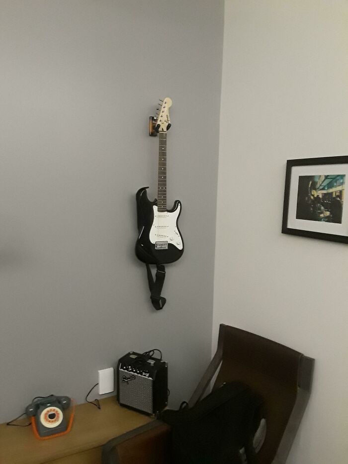 A black electric guitar mounted on a light gray wall above a small amplifier, a simple way to store an instrument.