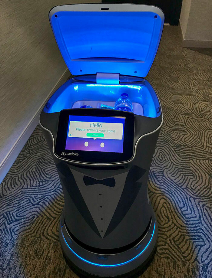 A delivery robot shaped like a person in a tuxedo with its lid open, showing a water bottle inside, solving everyday problems.
