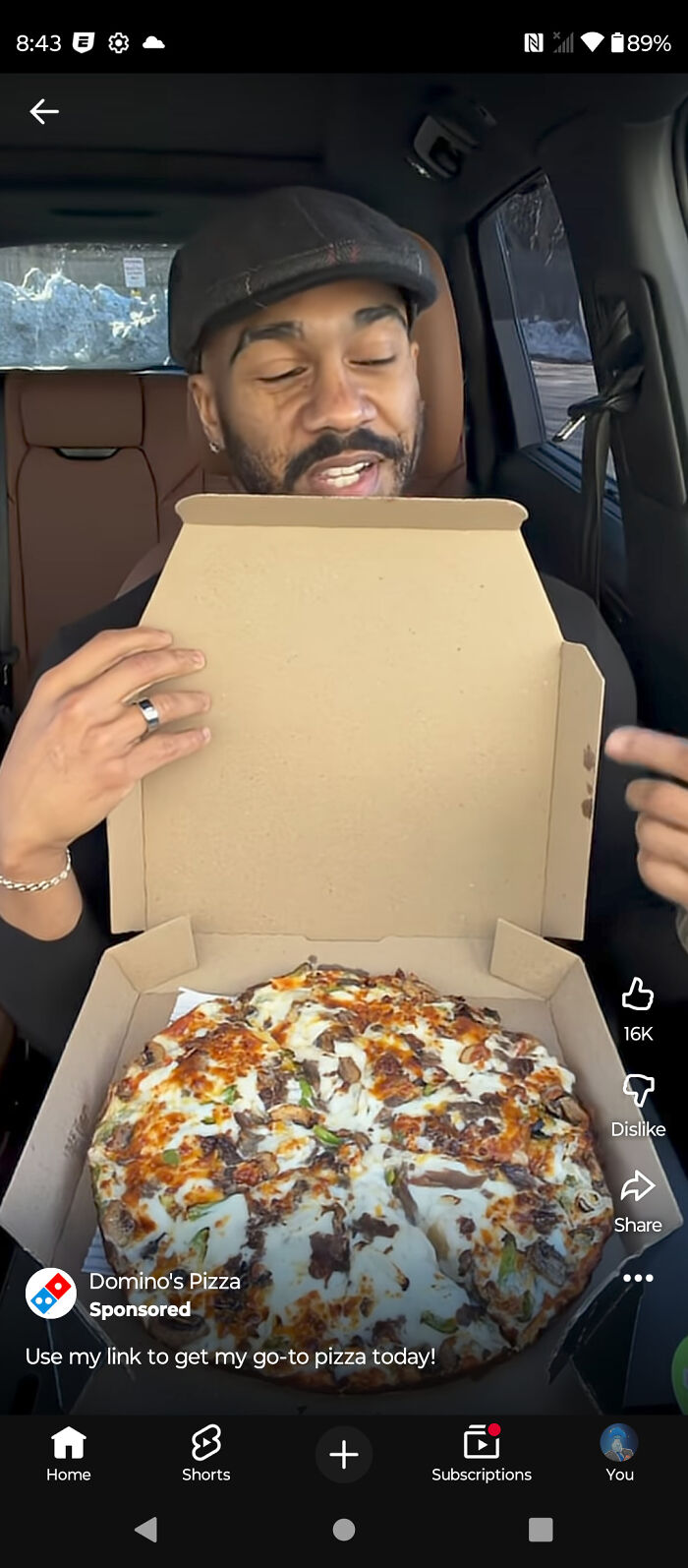 A man in a car opening a pizza box with a large pizza inside, a common sight in commercials.