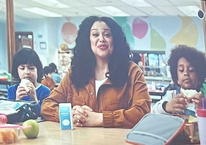 Woman in a brown jacket sitting with two children at a table, discussing commercials people can't stand.