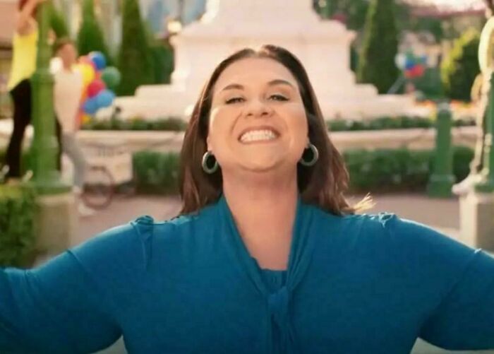 A woman smiling widely, arms outstretched, expressing joy in a commercial setting, featuring an energetic scene people can't stand.