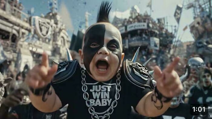 A baby with a mohawk and face paint, dressed in a football-themed punk outfit, from a commercial.