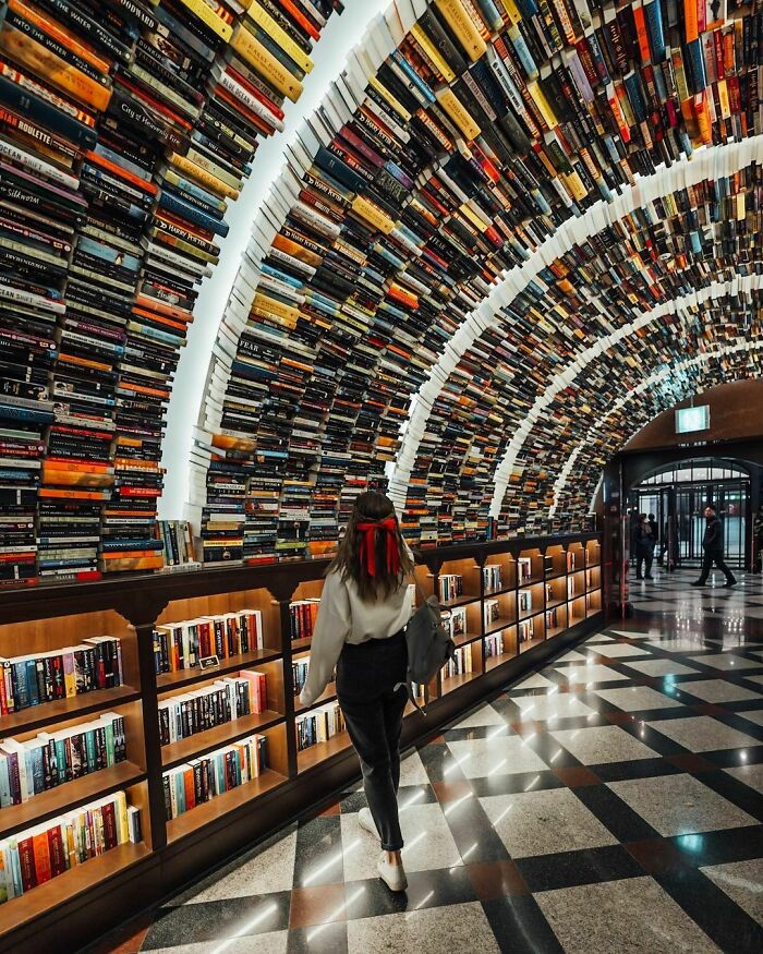 A woman walking through a library with an arched ceiling made entirely of books, a surprisingly simple and genius idea for design.