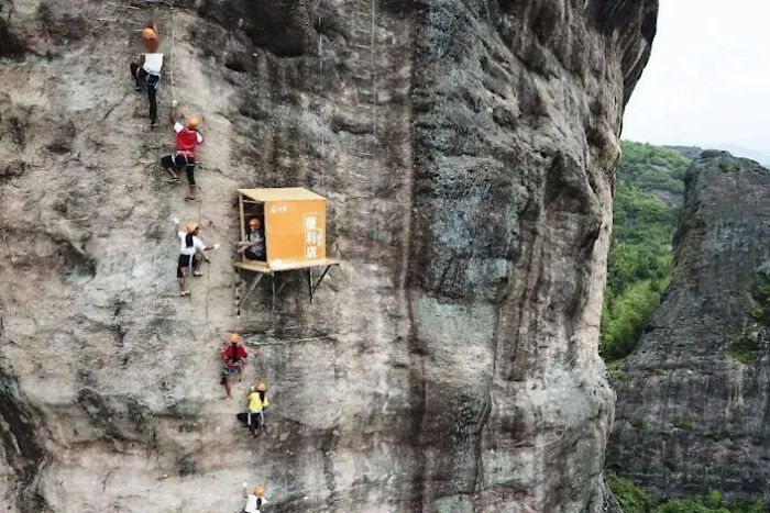Climbers on a cliff face, with a small hut built into the rock, a surprisingly simple and genius idea for an extreme business.