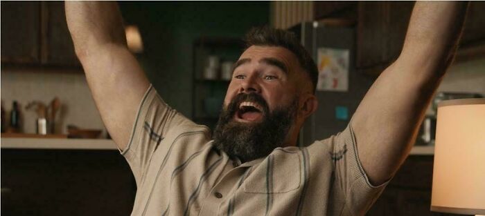 A man with a beard and short hair raises his arms in celebration, clearly enjoying a commercial.
