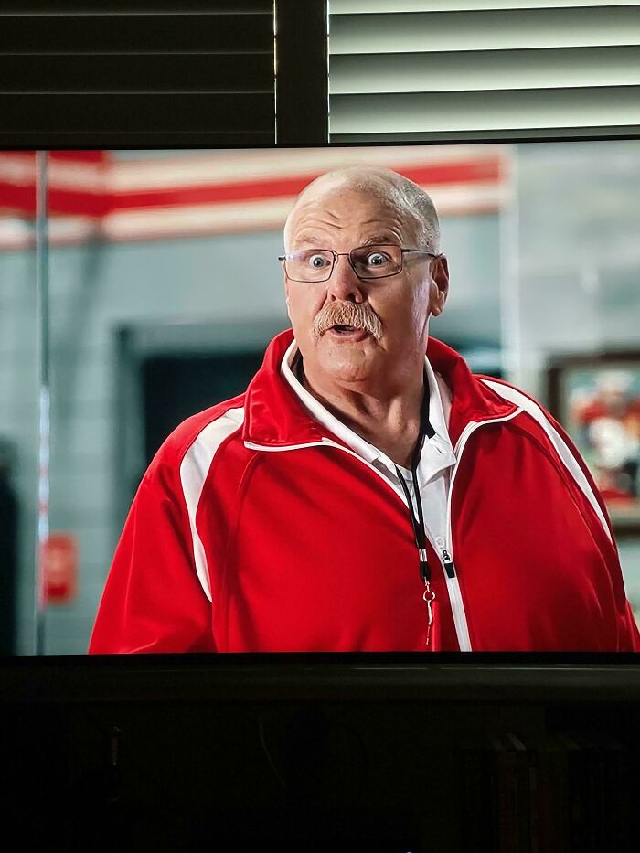 A man with a mustache and glasses, wearing a red jacket with white stripes, has a surprised expression on his face in a commercial.